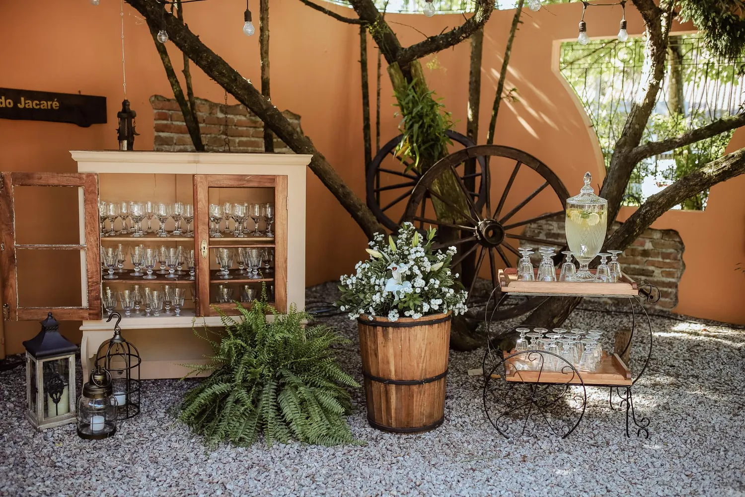 Cristaleira com taças e barril de flores no jardim, sob a figueira